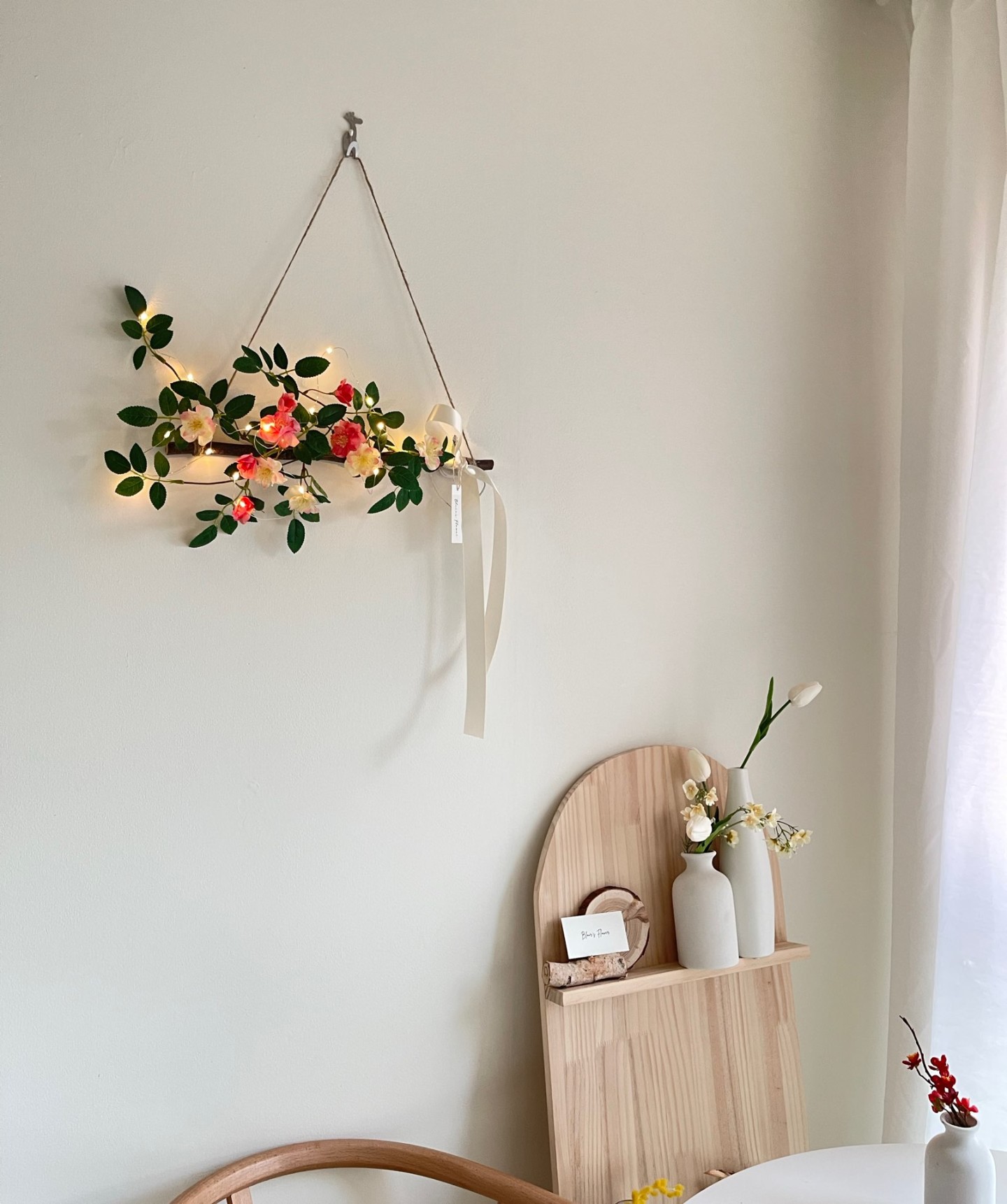 A garland with pink flowers hanging on a wall above a decorative pottery arraignment